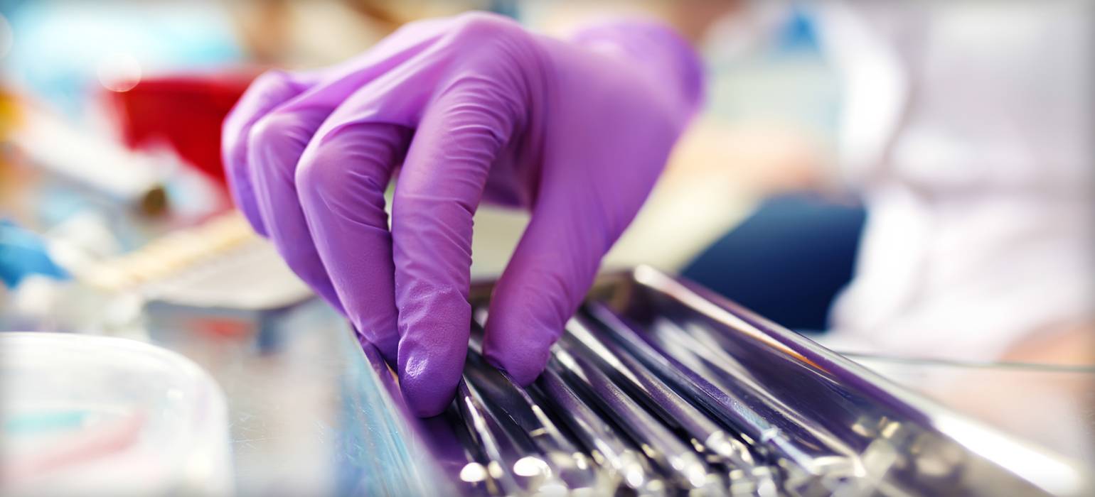 Hand in rubber glove handling dental tools